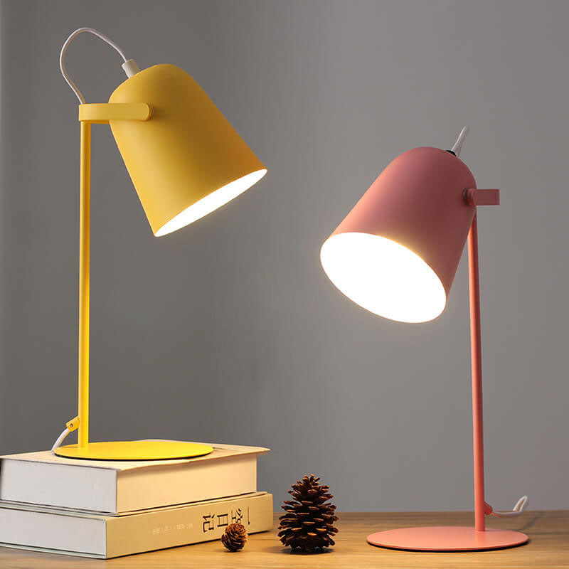 Yellow and pink desk lamps on a wooden surface with books and pine cones.