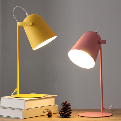 Yellow and pink desk lamps on a wooden surface with books and pine cones.