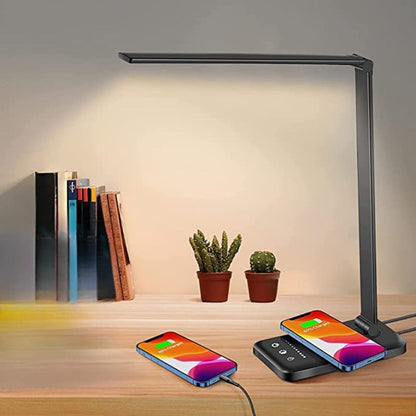 Desk lamp with wireless charging pad on a wooden surface with books and plants.