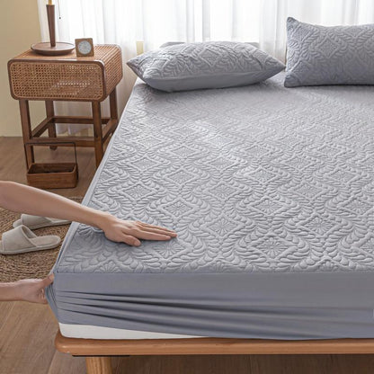 Person adjusting a gray quilted mattress cover on a bed in a bedroom.