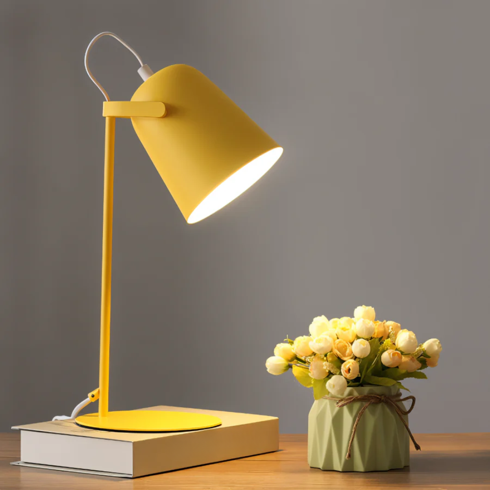 Yellow desk lamp on a wooden surface with a small potted plant against a gray background