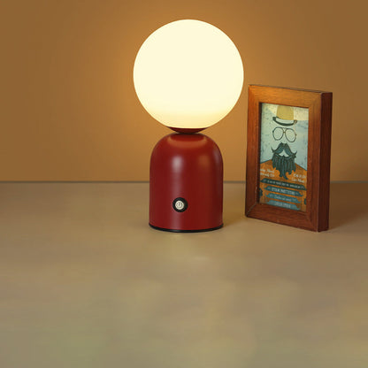 Red table lamp with a white globe shade next to a framed picture on a beige surface.