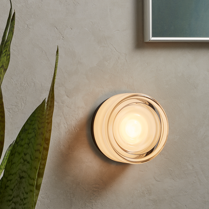 Black base Round wall light fixture on a textured wall with a plant leaf in the foreground