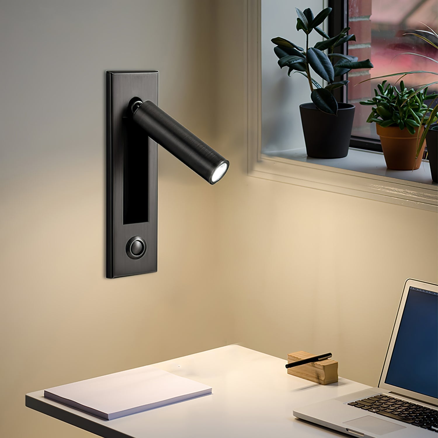 Black wall-mounted light fixture on a wall with a desk and laptop in the foreground