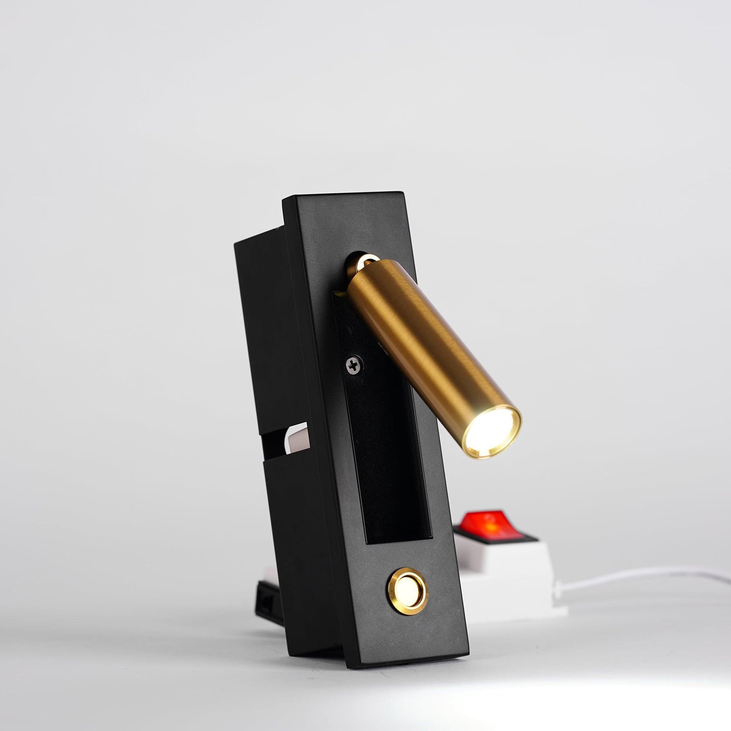 Modern wall-mounted light fixture with black base and gold cylindrical lamp on a white background