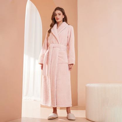 Woman wearing a pink robe in a room with a beige wall and white curtain.
