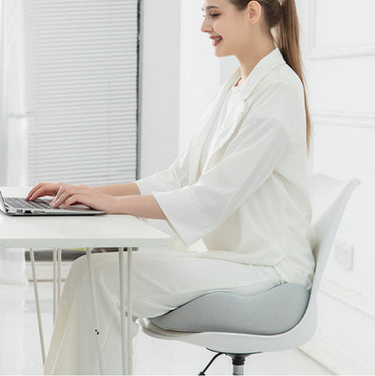 Woman in a white outfit sitting at a desk with a laptop in a bright room.