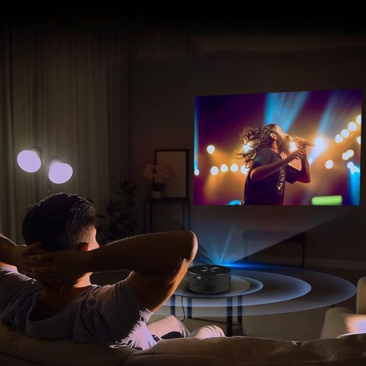 Person watching a concert on a large screen TV in a dimly lit room.