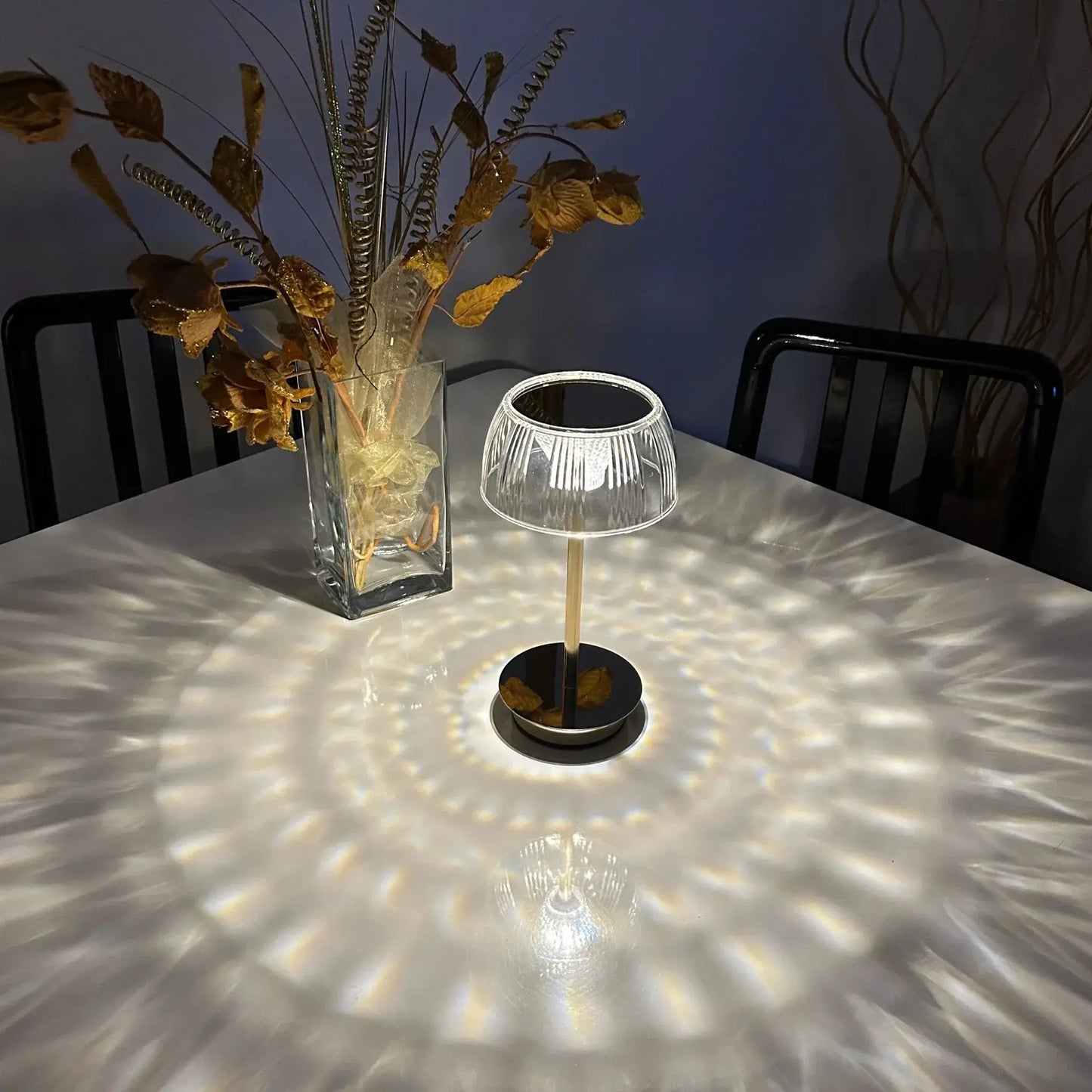 Small table lamp casting a pattern on a table with a vase of dried flowers in the background.