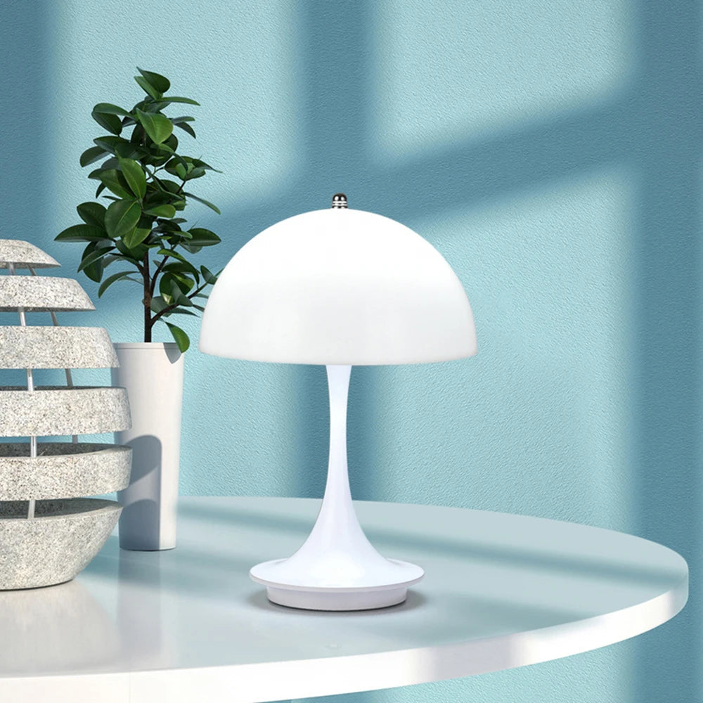 White table lamp on a round white table with a plant and decorative item against a light blue wall.