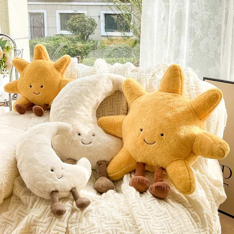 Two plush suns and a plush moon on a textured surface with a window in the background.
