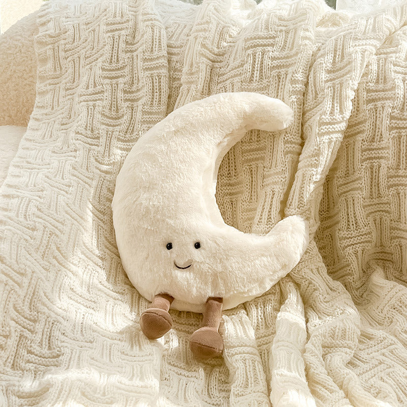 Plush moon-shaped toy with a smiling face on a textured beige blanket