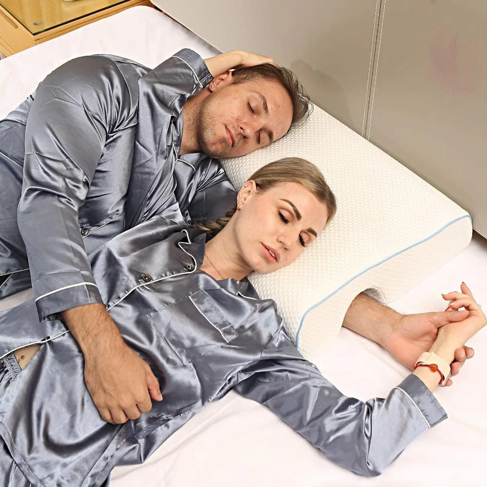 Man and woman in satin pajamas lying on a bed with a white pillow.