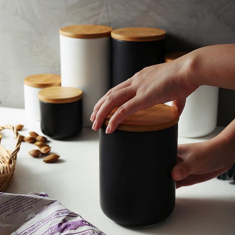 Person holding a black container with a wooden lid on a light surface.