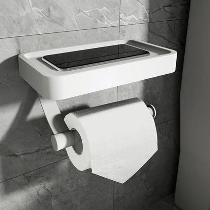White wall-mounted toilet paper holder with a black rectangular object on a tiled bathroom wall.